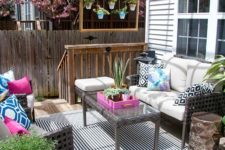 a bright boho deck with wicker furniture, planters with greenery and blooms, a bright blue chandelier and printed pillows