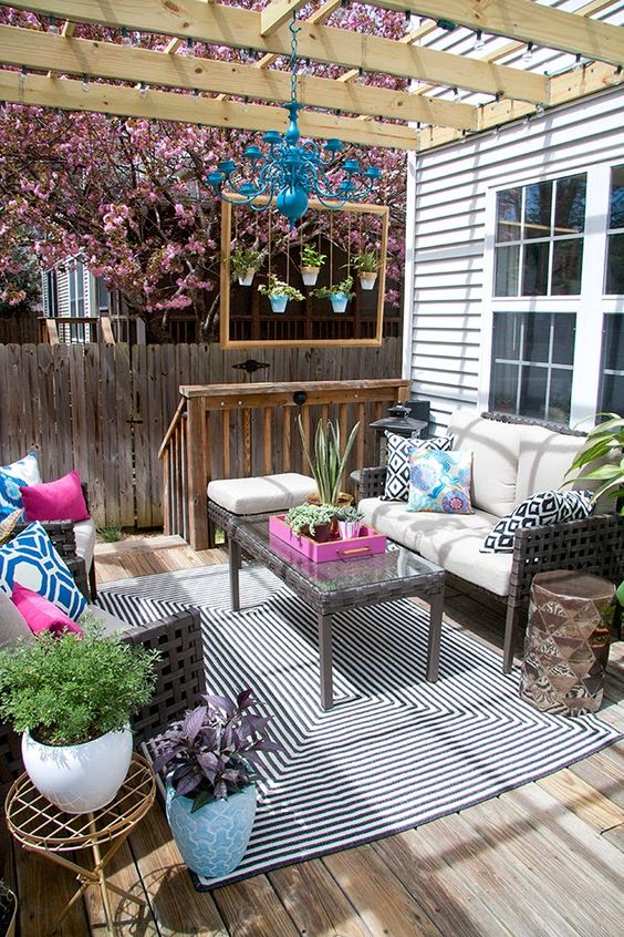 a bright boho deck with wicker furniture, planters with greenery and blooms, a bright blue chandelier and printed pillows