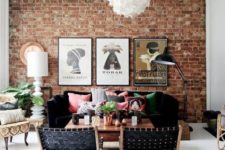 a bright boho living room with a red brick statement wall, black furniture and colorful pillows