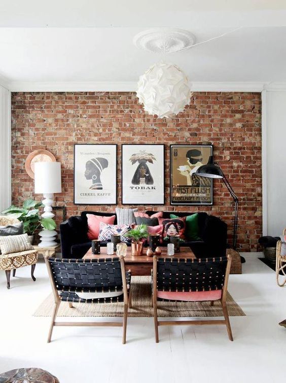 a bright boho living room with a red brick statement wall, black furniture and colorful pillows
