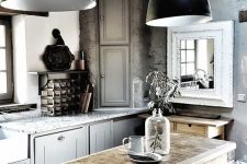 a catchy kitchen with concrete walls, light grey cabinets, neutral stone countertops, black pendant lamps and a vintage wooden kitchen island