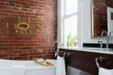 a chic bathroom done in white and with contrasting touches – a red brick wall and a rich toned vanity