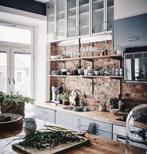 a chic kitchen with blue cabinets, light-colored countertops and a red brick wall looks very refreshing