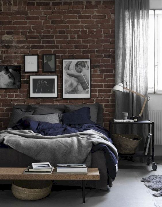 a chic moody bedroom with a faux brick wall, a cork bench, a dark bed and a monochromatic gallery wall