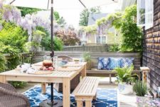 a colorful deck with a printed rug, wooden furniture, potted greenery and blooms plus an umbrella