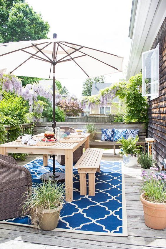 a colorful deck with a printed rug, wooden furniture, potted greenery and blooms plus an umbrella