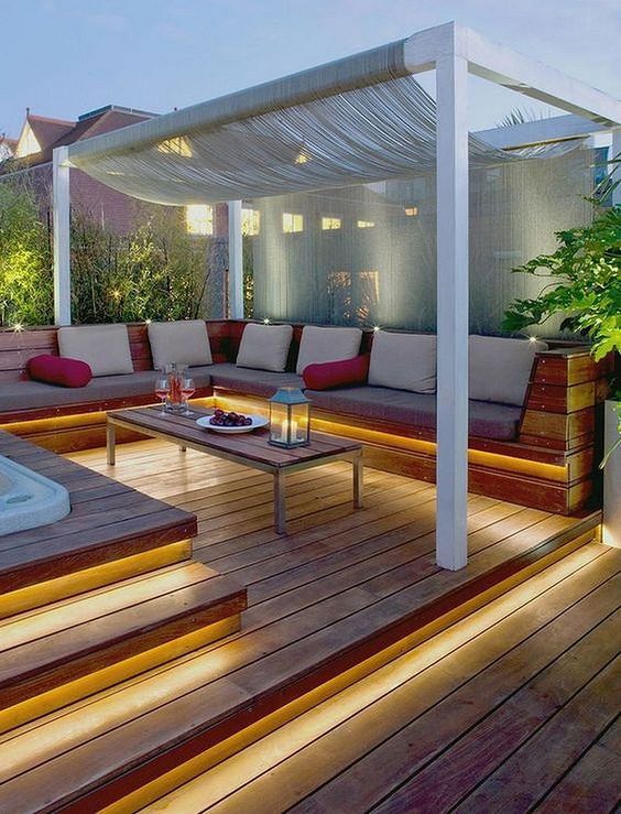 a contemporary deck with built-in lights in the steps and a built-in bench, a coffee table and a canopy over the sitting zone
