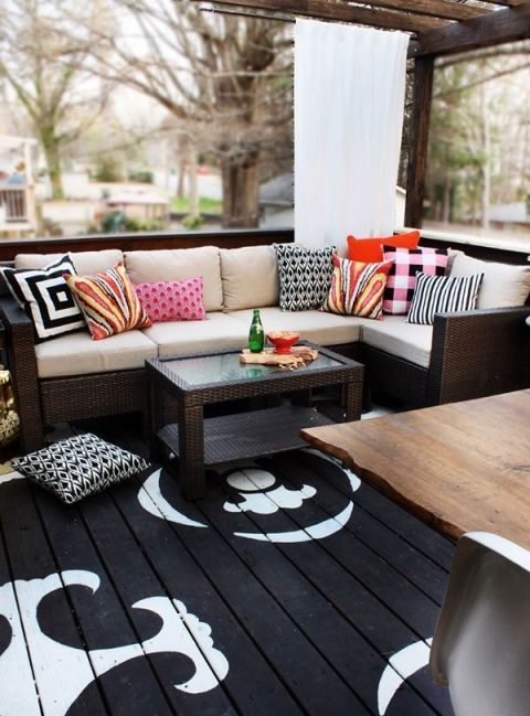 a contrasting deck with a black and white floor, dark wicker furniture and colorful pillows