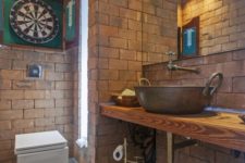a creative bathroom done with bricks, metal faucets and a sink and a large mirror looks very quirky