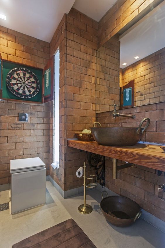 a creative bathroom done with bricks, metal faucets and a sink and a large mirror looks very quirky