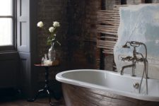 a dark industrial bathroom with red brick walls, dark wooden floora and a chic metal bathtub for a refined look