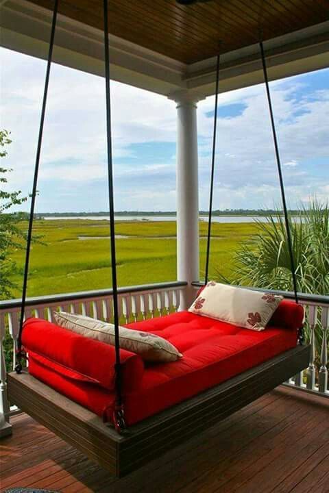 a dark stained wooden hanging bed on ropes with bright bedding and a gorgeous view to enjoy
