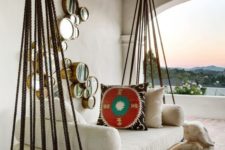 a hanging bed with white cushions and pillows on ropes looks very Mediterranean-like