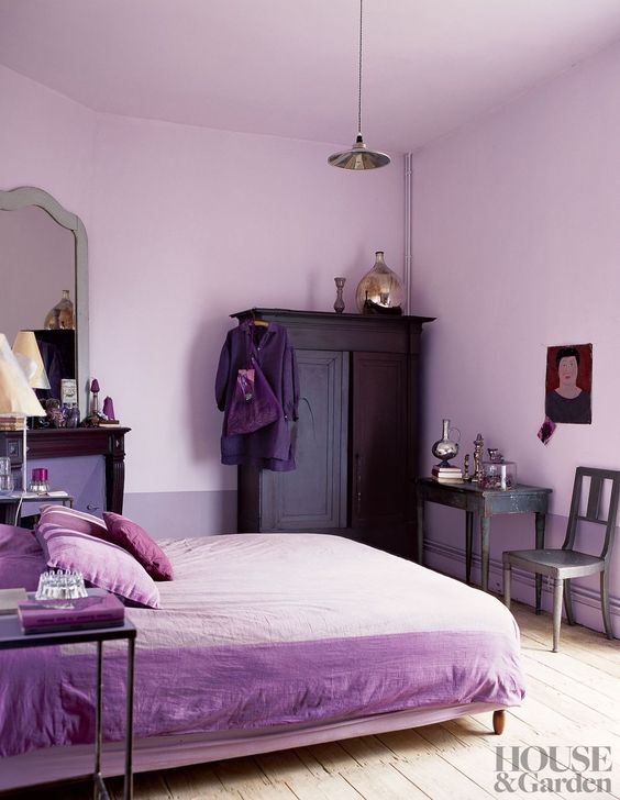 a lavender bedroom with dark stained furniture, a vintage table and chair, shiny metallic touches and a mirror
