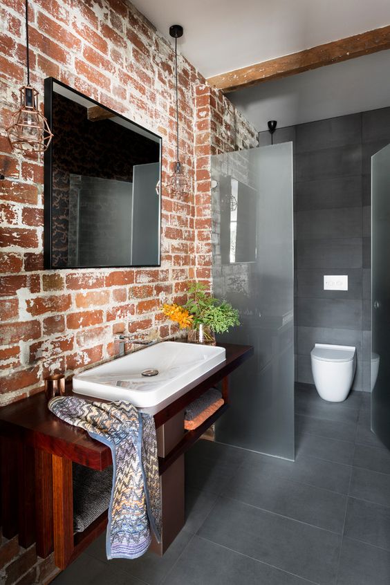 a minimalist bathroom done in greys with a brick wall that adds character and interest to the space