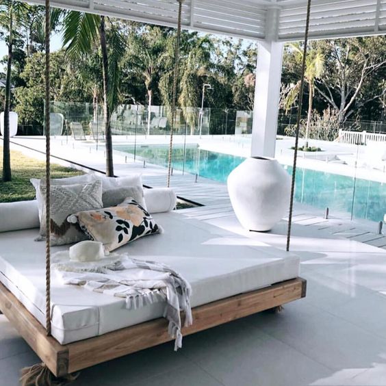 a modern hanging bed on ropes with pillows and blankets is a great idea for an outdoor tropical space