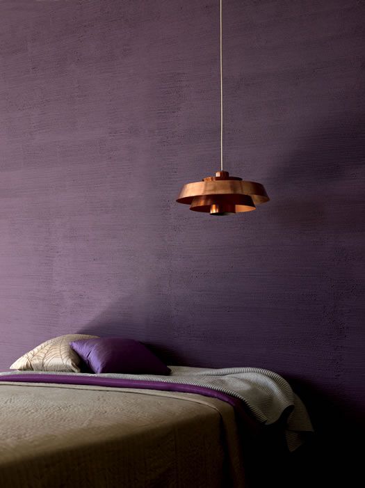 a moody bedroom with a textural purple wall, some purple and grey bedding and a copper pendant lamp over the bed