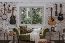 a music nook done with a whitewashed red brick wall and a refined green velvet sofa