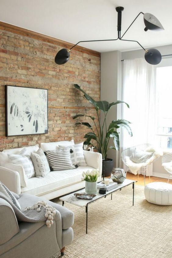 a neutral living room with potted greenery, black touches and an exposed brick wall for more drama