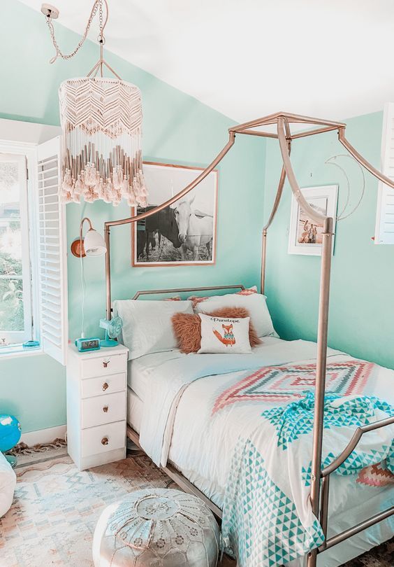 a pretty teen bedroom with aqua walls, a canopy bed with printed bedding, a nightstand, a boho tassel chandelier and a silver pouf