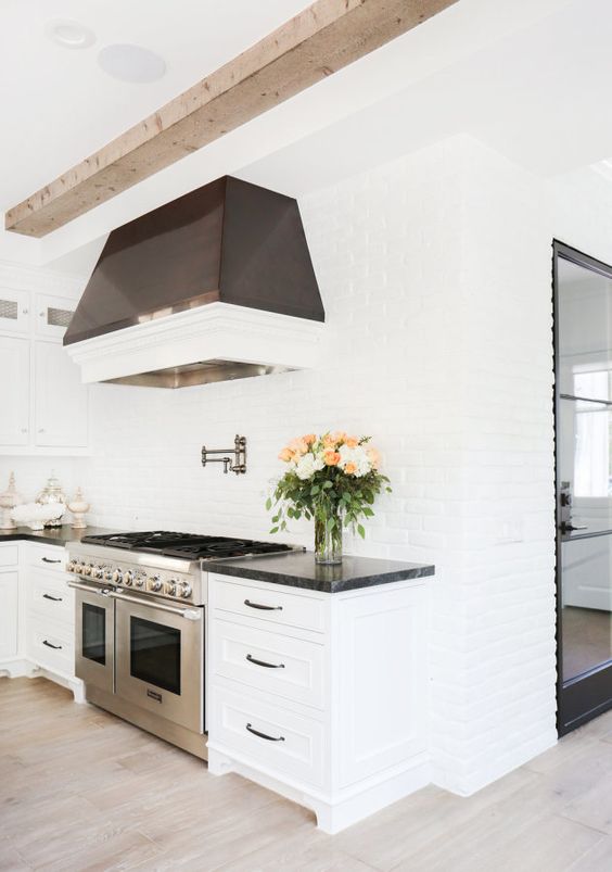 a purely white kitchen with white brick walls and a dark hood that stands out in a neutral space