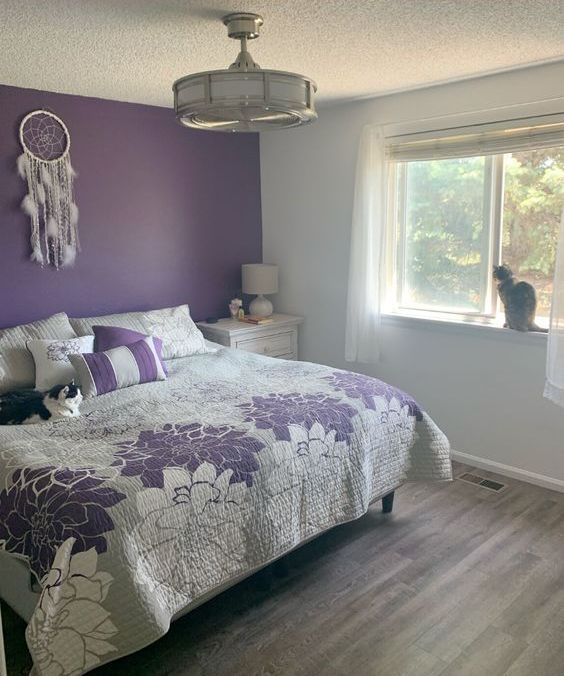 a purple and white bedroom with a statement wall, floral print bedding, a boho feather dream catcher and a drum chandelier