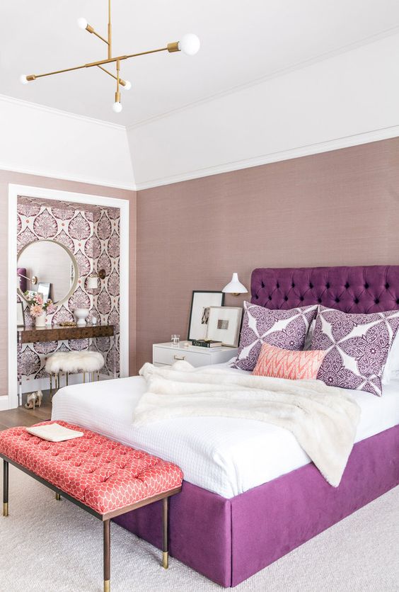 a refined bedroom with mauve walls, a wallpaper makeup niche, a round mirror, a metallic chandelier and a purple bed