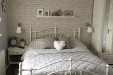 a romantic bedroom with a fau grey brick wall, a forged bed, some chic white furniture and lamps