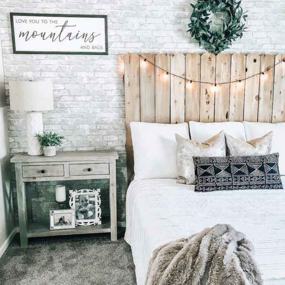 a rustic bedroom with a white fake brick wall, a reclaimed wood bed, lights and vintage furniture