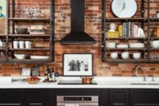 a rustic meets vintage kitchen with a red brick wall, black cabinets and blackened metal shelving units