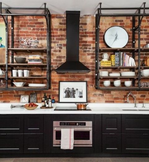 a rustic meets vintage kitchen with a red brick wall, black cabinets and blackened metal shelving units