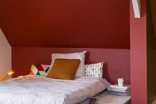 a small attic bedroom with a burgundy statement wall, a simple pallet bed, bright printed bedding and books