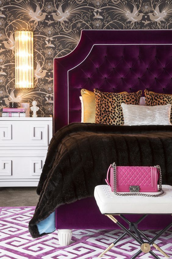 a sophisticated bedroom with printed wallpaper, a depe purple bed, a white bench, some wall sconces