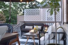 a striped deck with a dining and sitting space, some potted greenery, trees and blooms plus candle lanterns