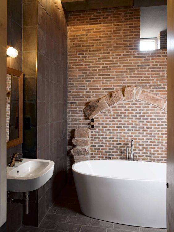 a unique bathroom done with chocolate brown tiles, a red brick wall and white appliances looks really outstanding
