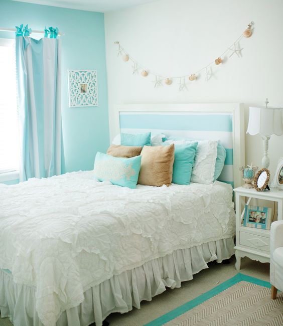 A vintage inspired bedroom with a turquoise accent wall, a bed with a striped headboard, pastel bedding, striped curtains