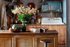 a vintage rustic kitchen with stained cabinets, a matching vintage kitchen island, pendant lamps and a dark metal hood