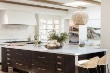 a white farmhouse kitchen with white stone countertops, wooden beams on the ceiling and a vintage black kitchen island with a white stone countertop