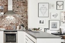 a white kitchen with grey countertops is refreshed and enlivened with a red brick wall