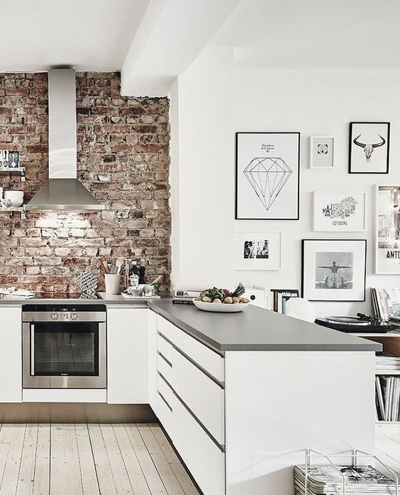a white kitchen with grey countertops is refreshed and enlivened with a red brick wall