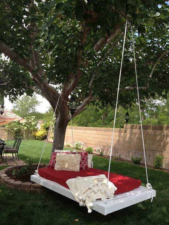 a whitewashed hanging bed on ropes with colorful bedding and pillows is a cool idea for outdoors