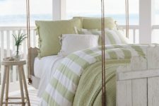 a whitewashed hanging wooden bed on ropes with a matching stool and green and white bedding looks very inviting