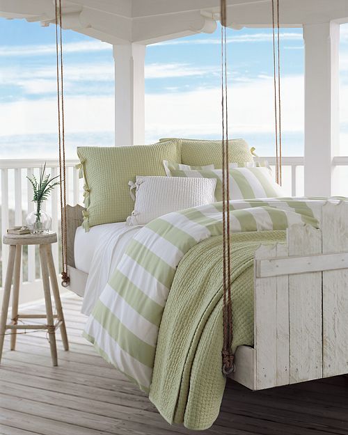 a whitewashed hanging wooden bed on ropes with a matching stool and green and white bedding looks very inviting