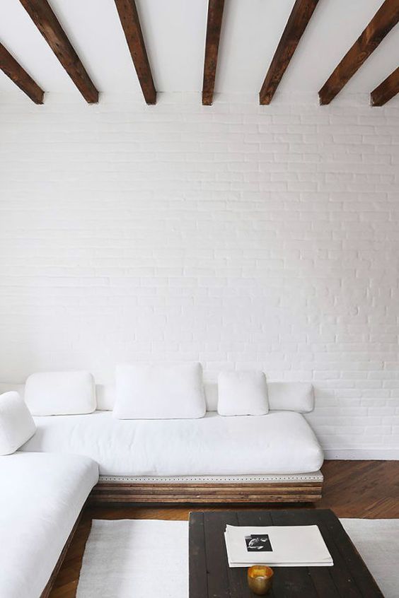 an airy and serene living room with white brick wlals, an L-shaped sofa