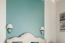 an elegant bedroom with a turquoise stripe on the wall and ceiling, a refined upholstered bed with colorful bedding, mismatching nightstands and a chic chandelier