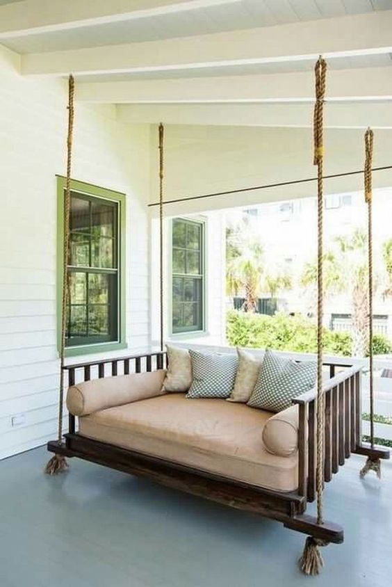 an outdoor hanging bed of dark stained wood, ropes with neutral and printed bedding and pillows is a great porch piece