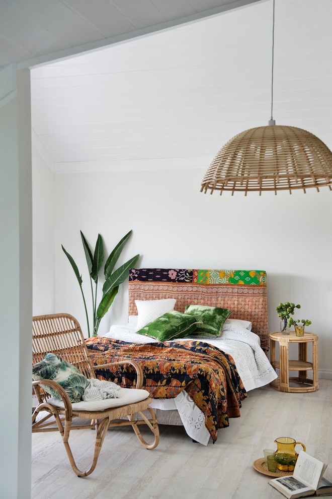 a bright tropical bedroom with a pink upholstered bed, a rattan chair, a wicker lampshade and bright bedding  (Bowerhouse)