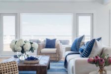 a beach living room with cool views, white upholstered and rattan furniture, a striped rug and printed pillows