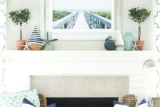 a beach mantel with mini boats, starfish, greenery in pots, a rope ball and a sea pier artwork