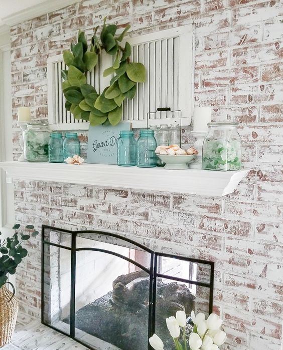 a beach mantel with turquoise jars, seashells in a bowl, jars with seaglass and a greenery wreath